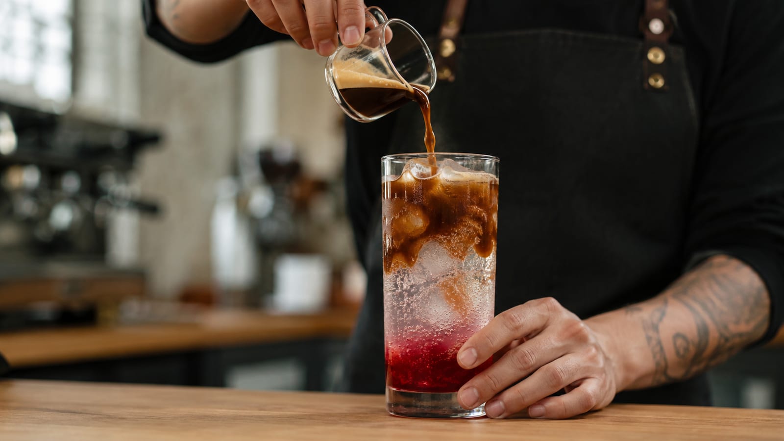 Pouring espresso over tonic water and cranberry juice in a café setting