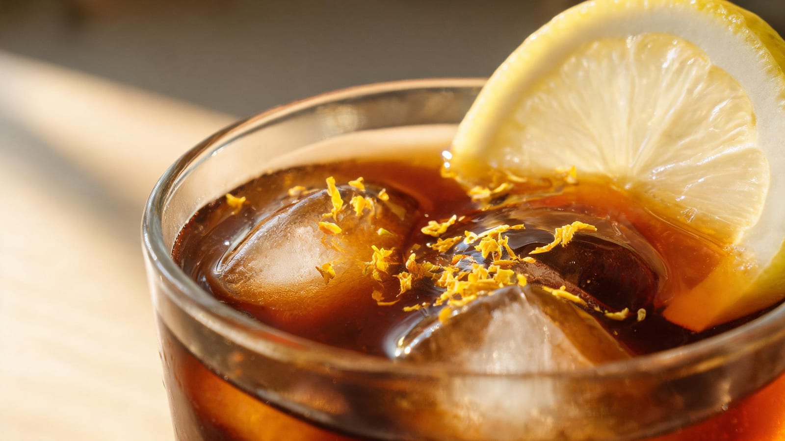 Close-up of dark lemon coffee with lemon zest resting on its surface and a garnished rim.