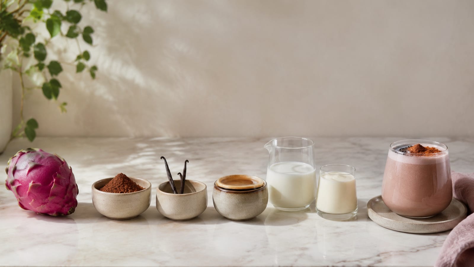 Pitaya, cacao, vanilla, espresso, and milk arranged beside a mixing bowl on a kitchen counter