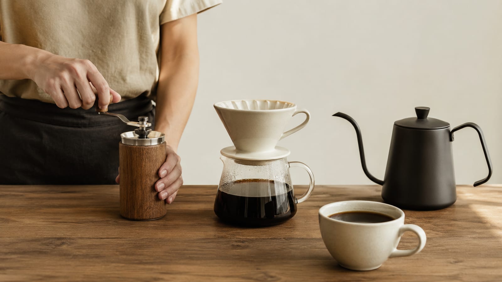 Home brewer preparing distinctive coffee beans with a grinder, kettle, and ceramic pour-over dripper