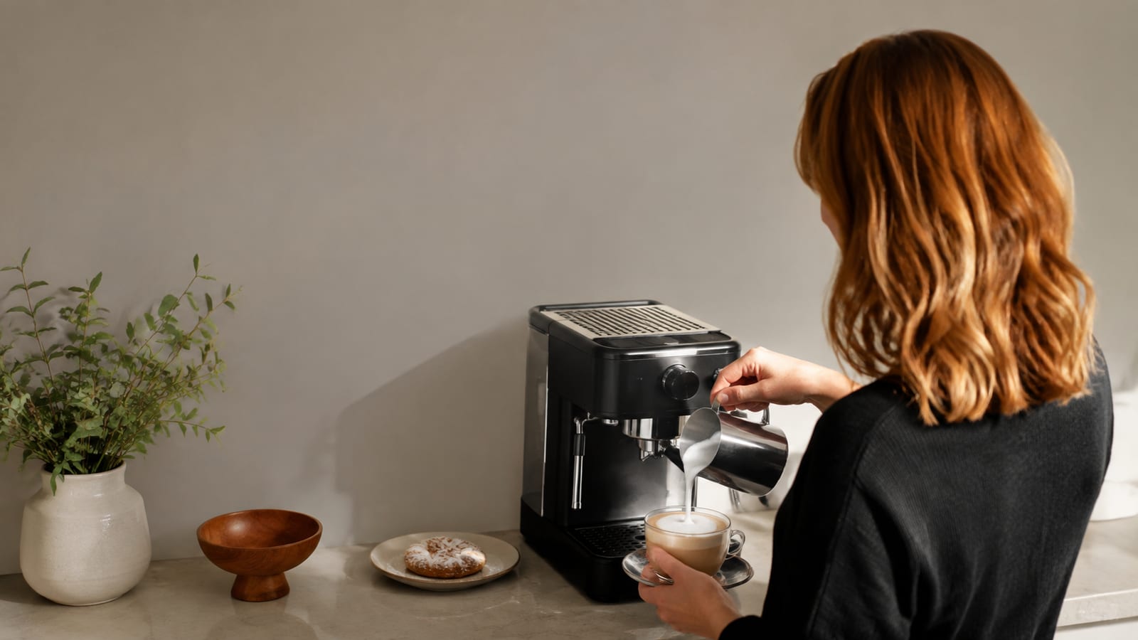 Home barista steaming milk into a Wiener Melange, viewed from behind in a bright kitchen