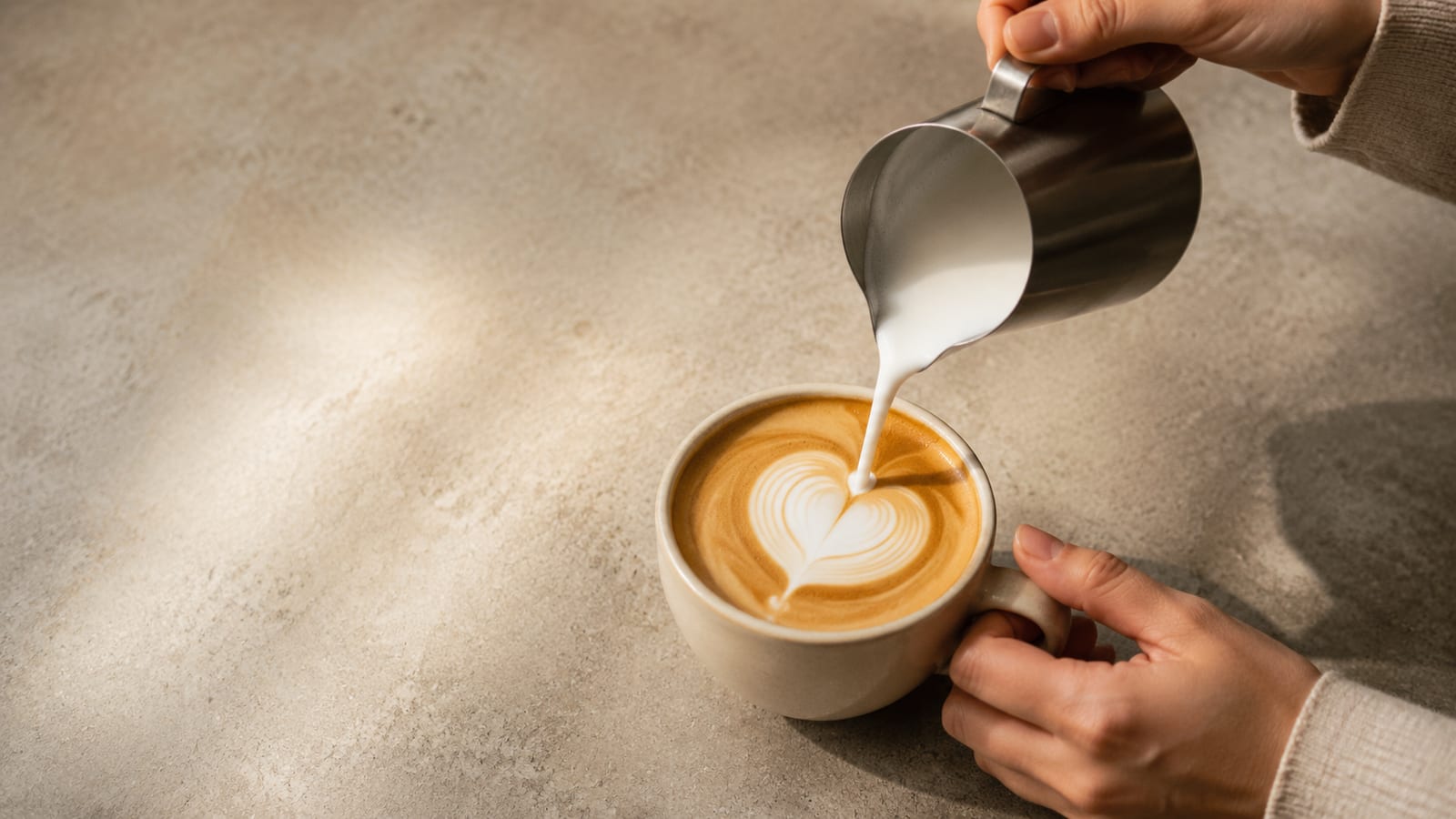 A clean heart pattern forms as frothed milk meets coffee in a plain cup